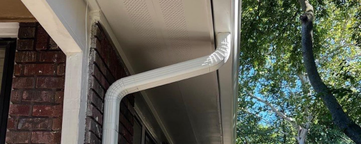 White vinyl gutters and downspout on brick house exterior with green trees