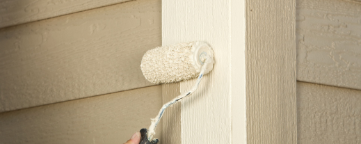Person painting exterior house trim with white paint using roller brush
