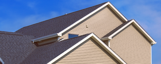 Modern beige vinyl siding house with dark asphalt shingle roof against blue sky