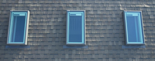 Three blue-framed windows on gray shingled roof of residential building