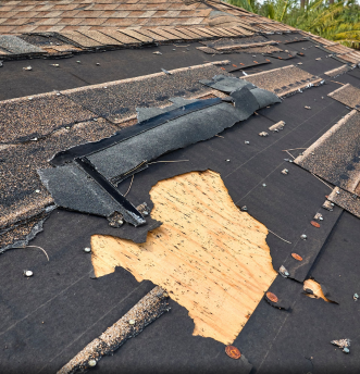 Damaged roof with torn shingles and exposed plywood decking after storm damage