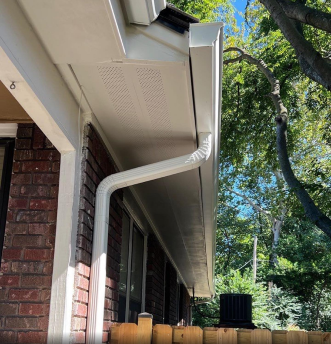 Modern brick house exterior with white gutters and green leafy trees overhead