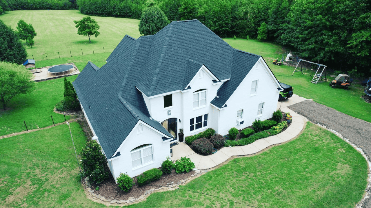 Aerial view of a large white house with a beautiful lawn and surrounding trees.