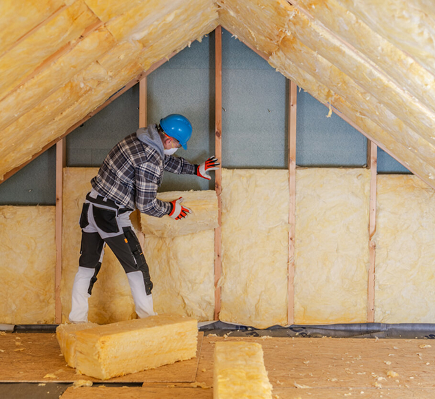 Worker insulating attic with fiberglass batts for energy efficiency.